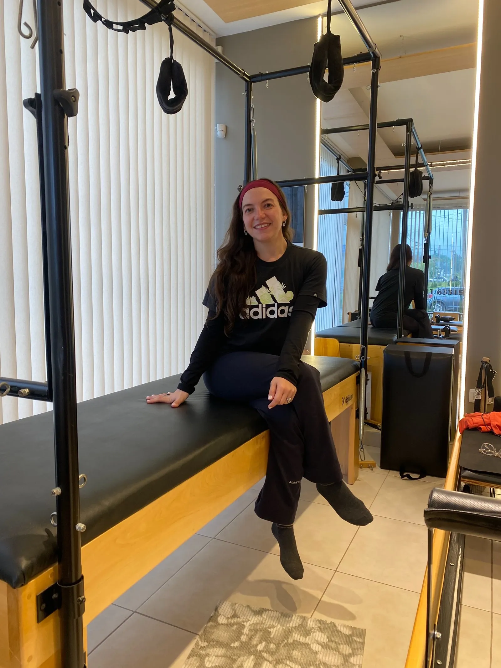 Alessandra, profesora de pilates, sentada y sonriendo sobre un cadillac de madera del estudio